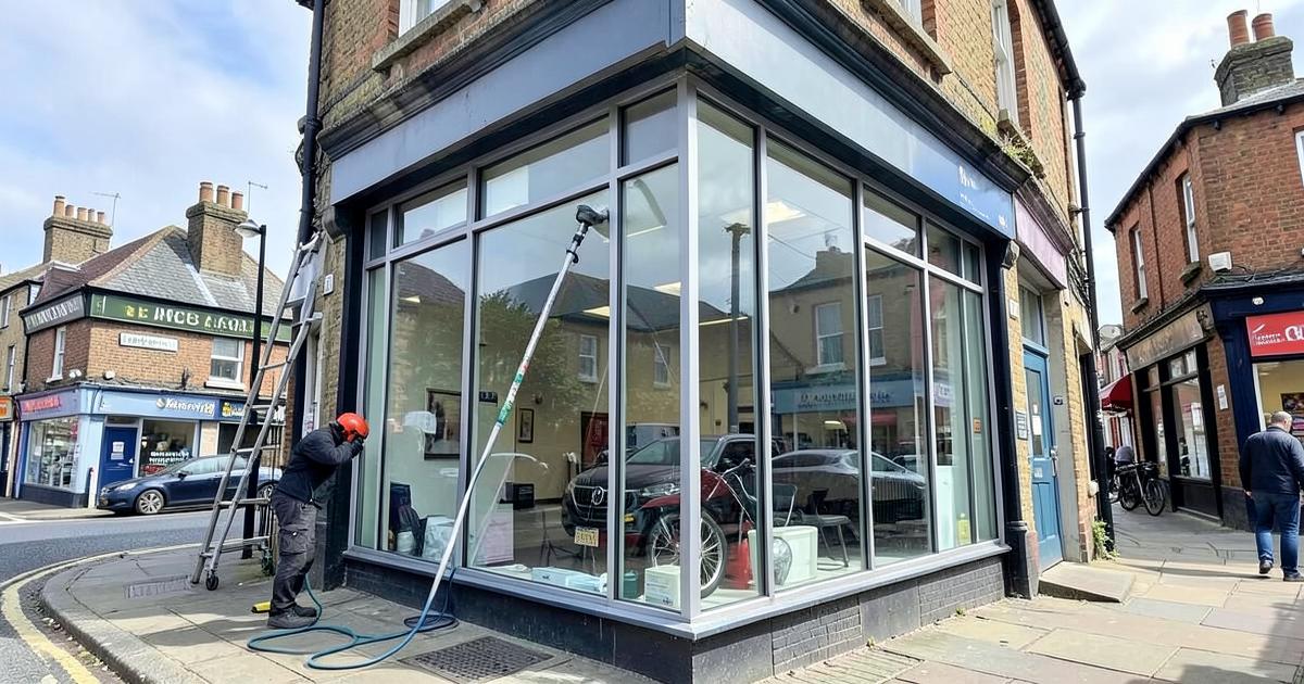 Window cleaner cleaning the glass frontage of a small UK high-street business